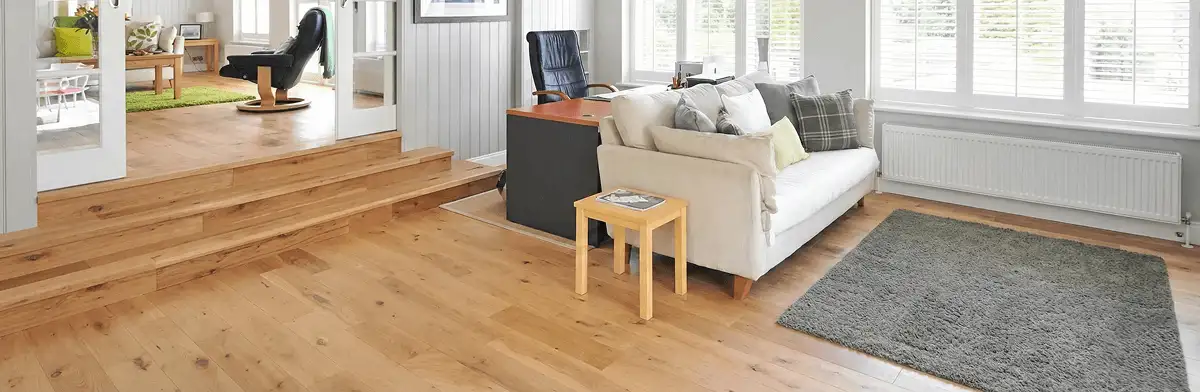 A modern living room with professionally installed laminate flooring, a beige sofa, a small side table, a gray rug, and large windows with white shutters in Honolulu, HI